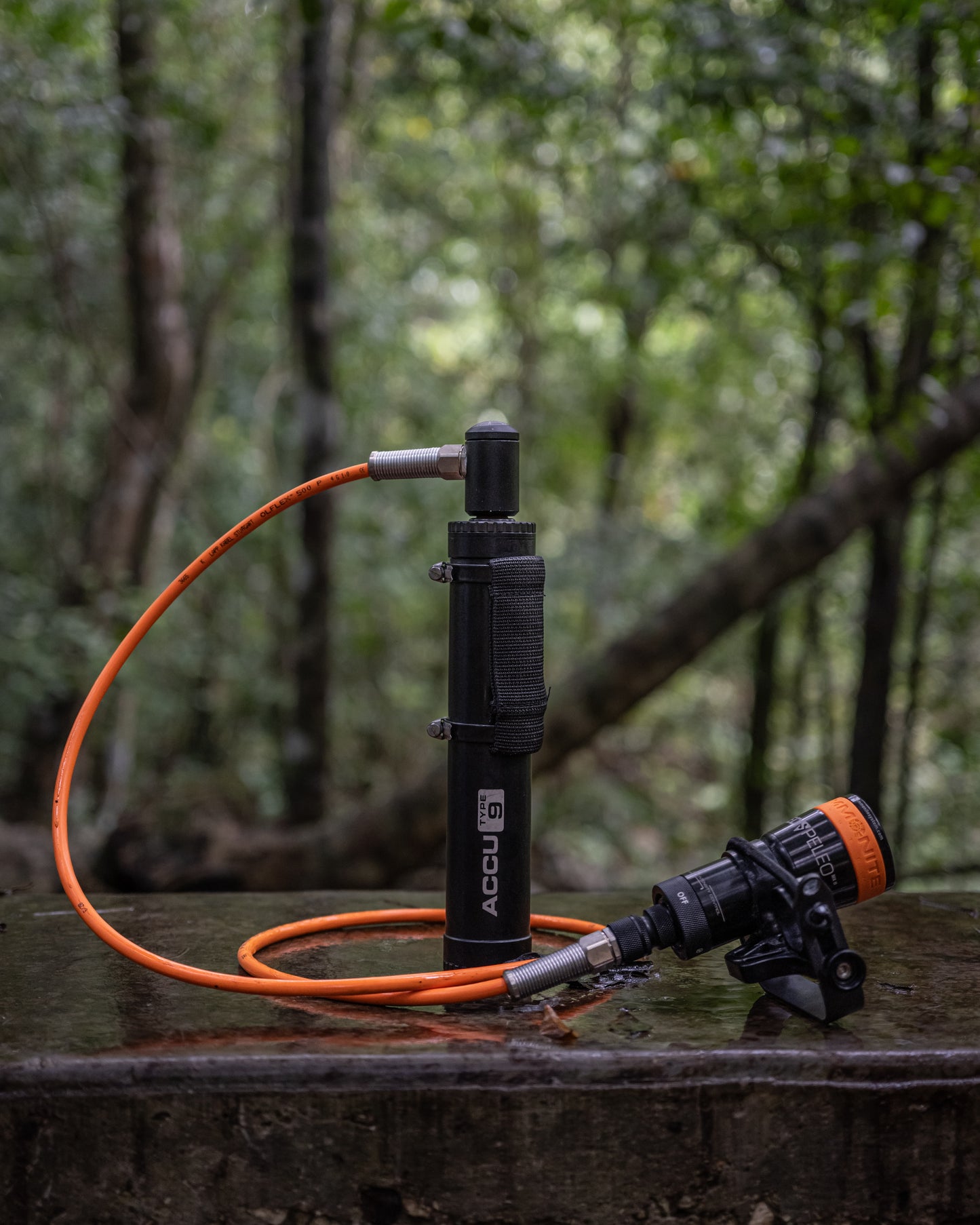 Umbilical diving light LED SPELEO MKII connected to a ACCU Type 9 battery from Ammonite System with a heavy duty cable, set on a wet stone surface in a forest setting.